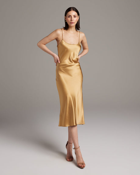 Woman wearing a gold slip dress against a plain background