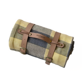 Roll-up picnic blanket with plaid pattern and brown straps on a light gray background