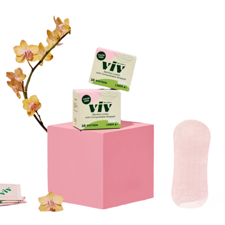 Viv product packaging on a pink stand with flowers and a single pad on a white background