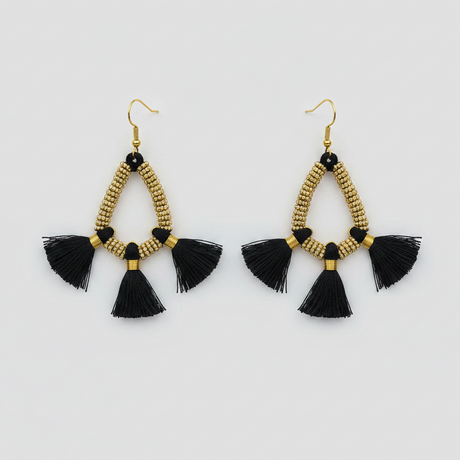 Pair of gold beaded earrings with black tassels on a light gray background