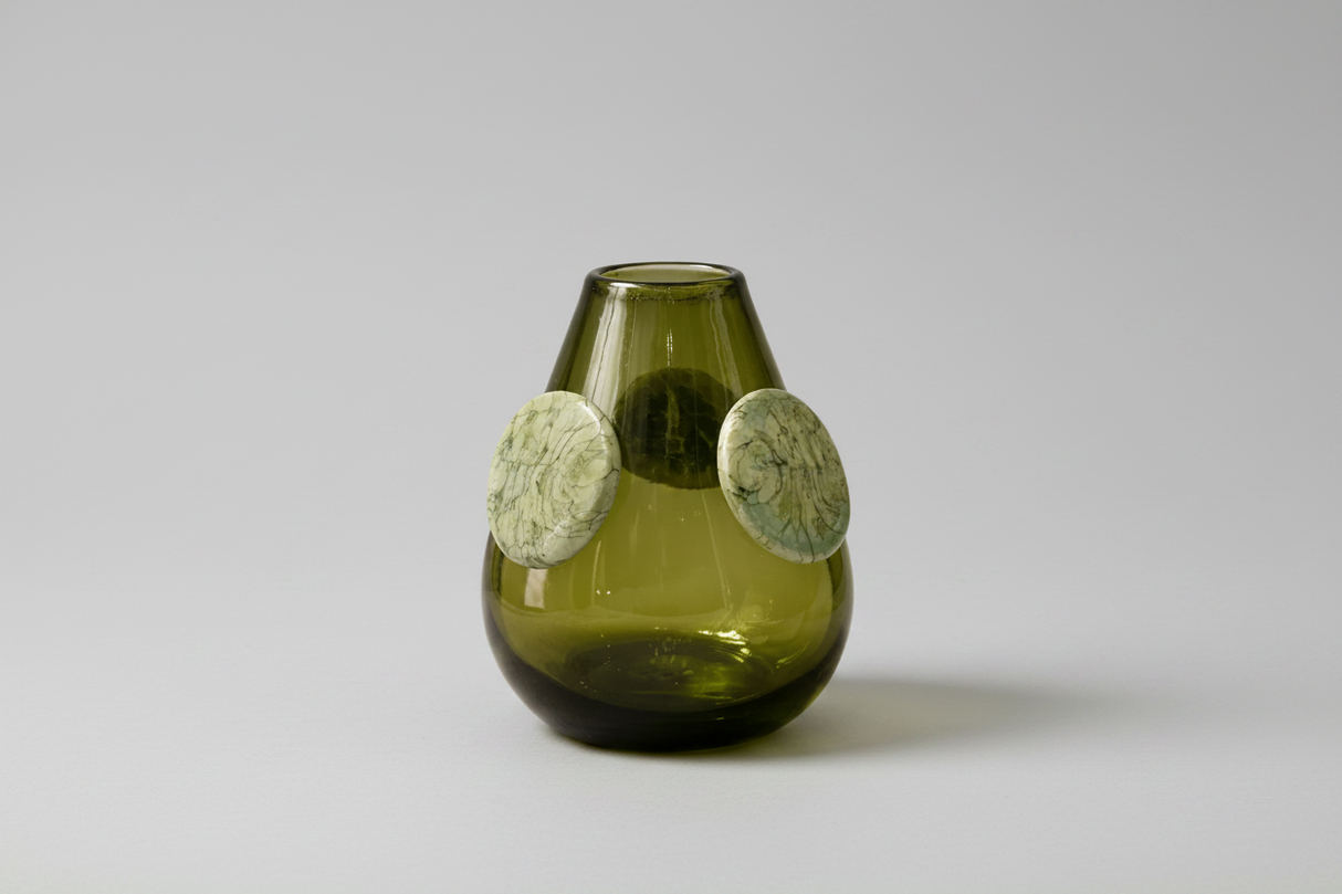 Green glass vase with circular decorations on a white background