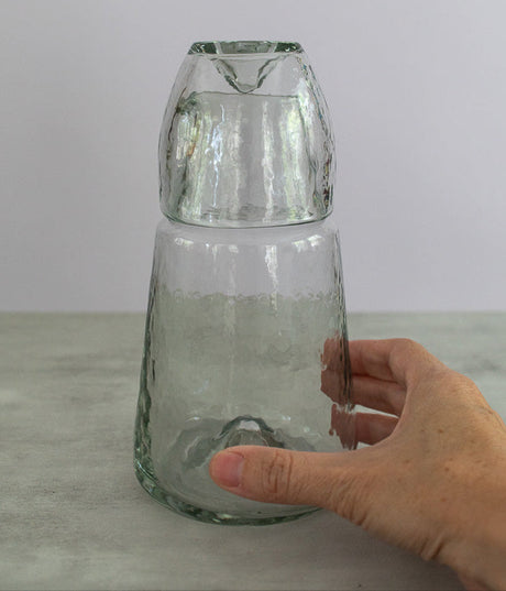 Hand holding a clear glass vase against a plain background