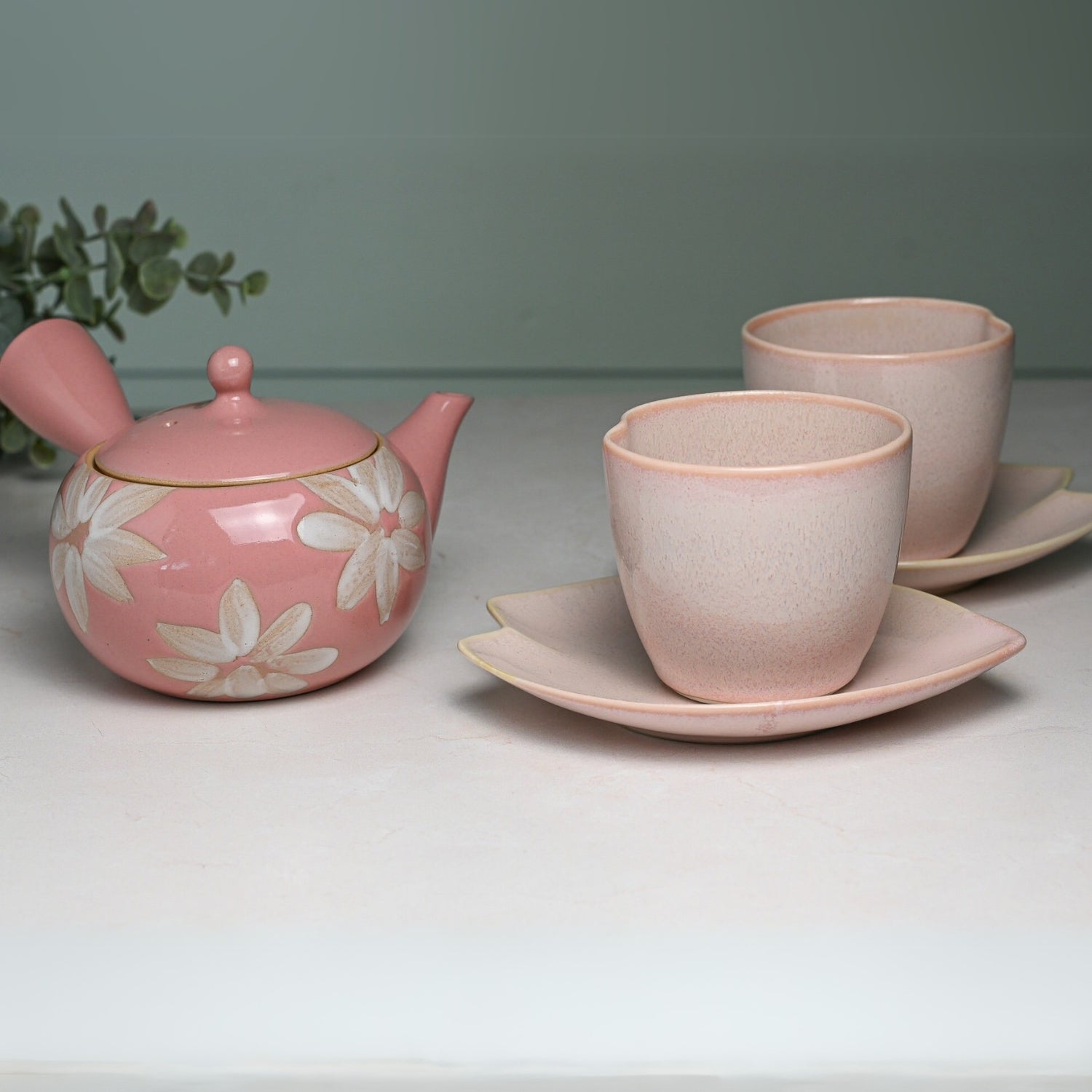 A Pink LOVE Ceramic Tea Cup with Saucer and a floral teapot are elegantly paired with two Japanese Ippuku-wan Tea Cups on matching saucers, all beautifully arranged on a white surface.