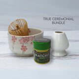 Discover the True Ceremonial Bundle: the Pink Sakura Flowers Ceramic Matcha Bowl, a bamboo whisk, whisk holder, and organic Japanese matcha tin. This elegant collection of matcha accessories is set against a light wood backdrop for timeless elegance.