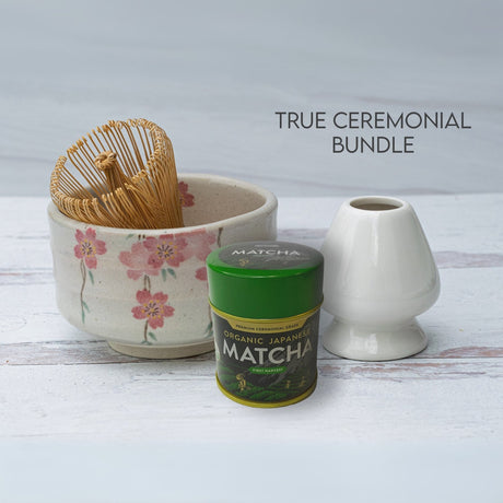 Discover the True Ceremonial Bundle: the Pink Sakura Flowers Ceramic Matcha Bowl, a bamboo whisk, whisk holder, and organic Japanese matcha tin. This elegant collection of matcha accessories is set against a light wood backdrop for timeless elegance.