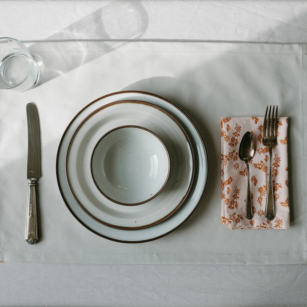 Dining table setting with white plates, silverware, and a floral napkin on a light gray surface.