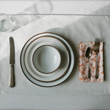Dining table setting with white plates, silverware, and a floral napkin on a light gray surface.