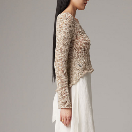 Woman wearing a textured beige sweater and white pants against a gray background