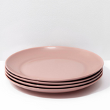 Set of four pink plates stacked on a white surface with a light gray background