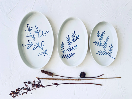 Three ceramic plates with blue leaf patterns on a white surface with dried plants. Süheyla Nesting Plates