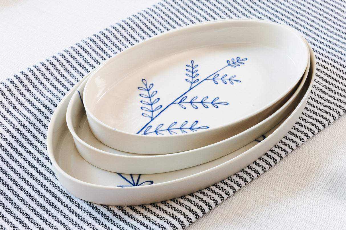 Set of white ceramic plates with blue leaf design on a striped fabric background. Süheyla Nesting Plates