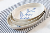 Set of white ceramic plates with blue leaf design on a striped fabric background. Süheyla Nesting Plates