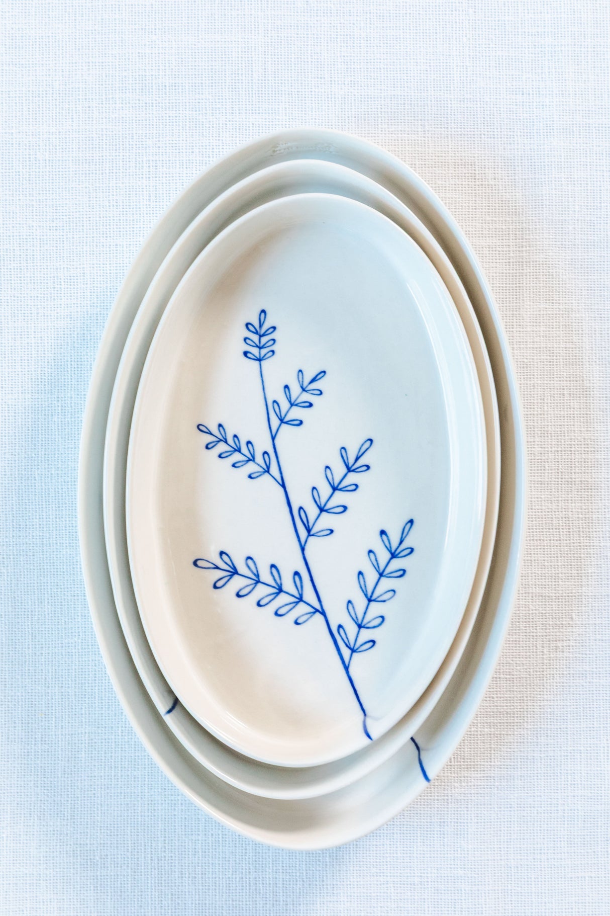 Set of white ceramic plates with blue leaf design on a light blue background. Süheyla Nesting Plates