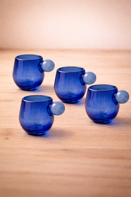 Four blue glass tumblers with unique designs on a wooden surface