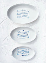 Three white plates with blue fish illustrations on a textured white background. Sardines Nesting Plates