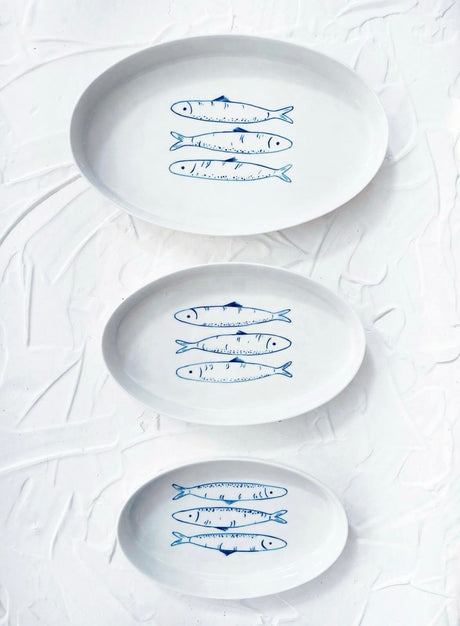 Three white plates with blue fish illustrations on a textured white background. Sardines Nesting Plates