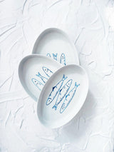 Three white plates with blue fish illustrations on a textured white background. Sardines Nesting Plates