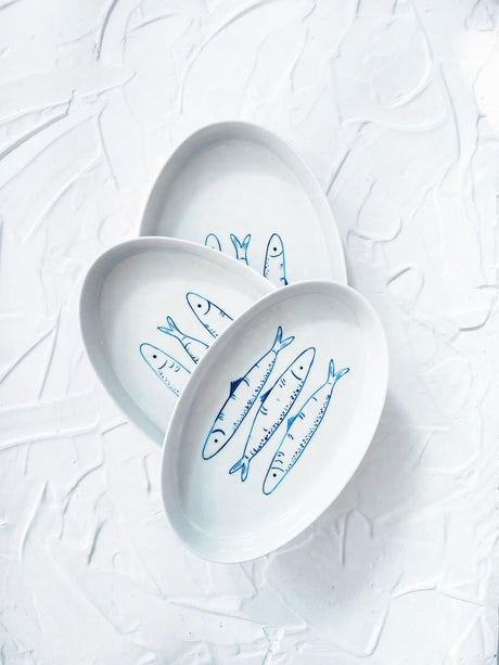 Three white plates with blue fish illustrations on a textured white background. Sardines Nesting Plates