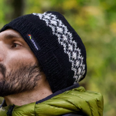 Person wearing a black knit beanie with a patterned edge, outdoors.