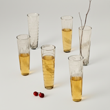 Set of tall glasses with a textured design, filled with a yellowish liquid, on a white background.
