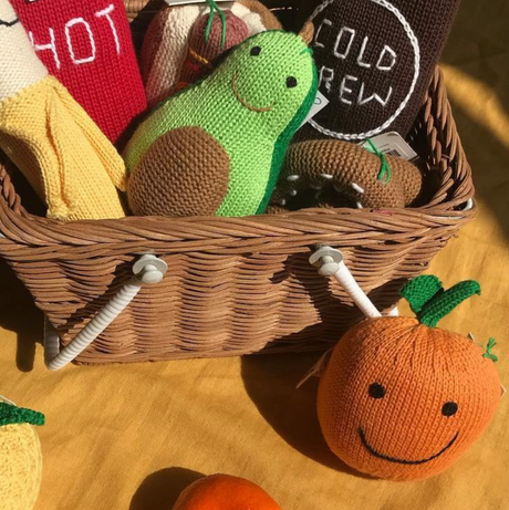 Basket with knitted toys including a green turtle, brown bear, and orange pumpkin on a wooden surface.
