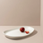 White oval platter with two red plums on a beige background