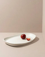 White oval platter with two red plums on a beige background