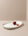 White oval platter with two red plums on a beige background
