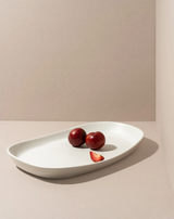 White oval platter with three red plums on a beige background