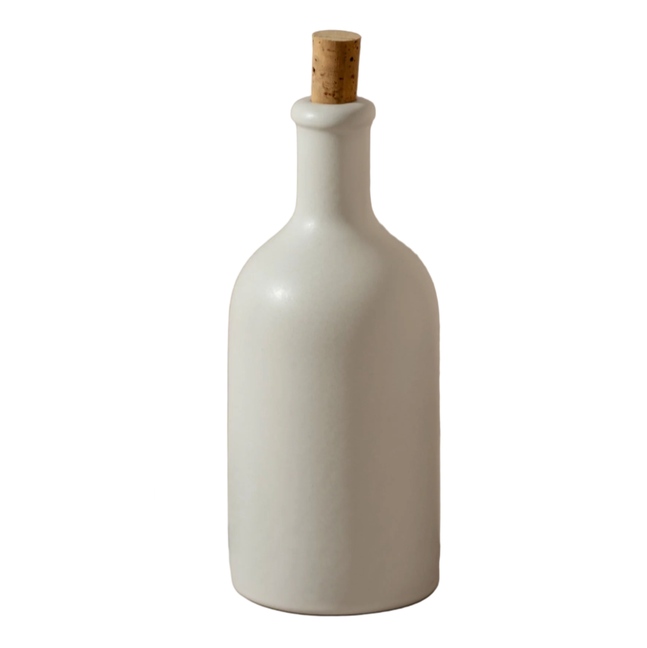 White ceramic bottle with cork stopper and two kiwis on a white background