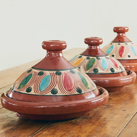 Three ceramic tagines with colorful patterns on a wooden surface