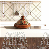Kitchen counter with a ceramic tagine and metal utensils against a tiled wall.