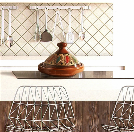 Kitchen counter with a ceramic tagine and metal utensils against a tiled wall.