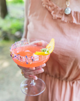 Person holding a cocktail with a lemon wedge outdoors