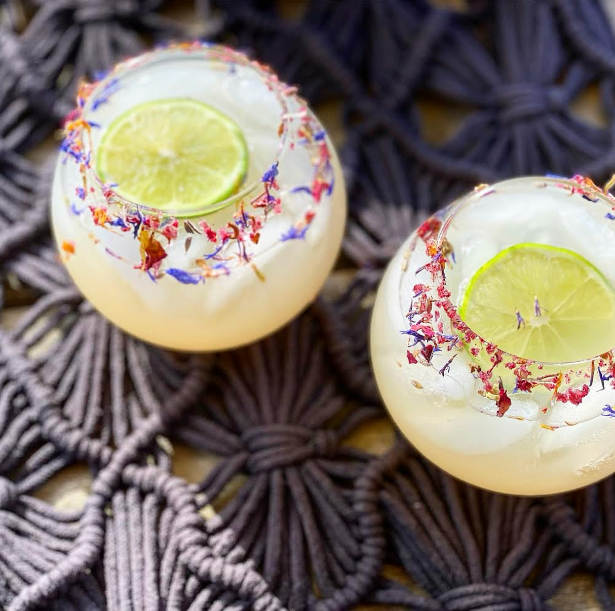 Two glasses of lemonade with lime slices and floral rim on a textured surface