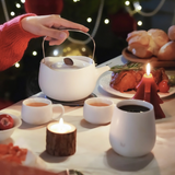 Person pouring tea from a white teapot into cups on a festive table with Christmas decorations.