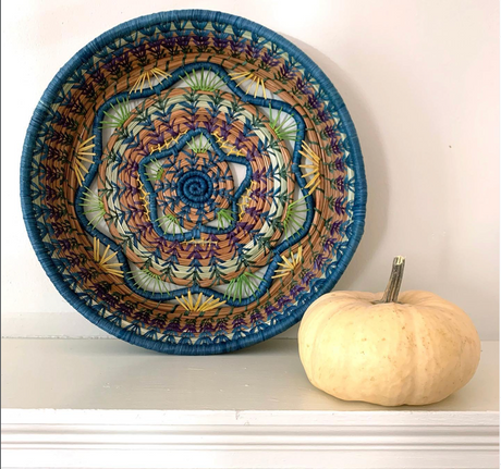 Decorative woven bowl with geometric pattern next to a small pumpkin on a white surface