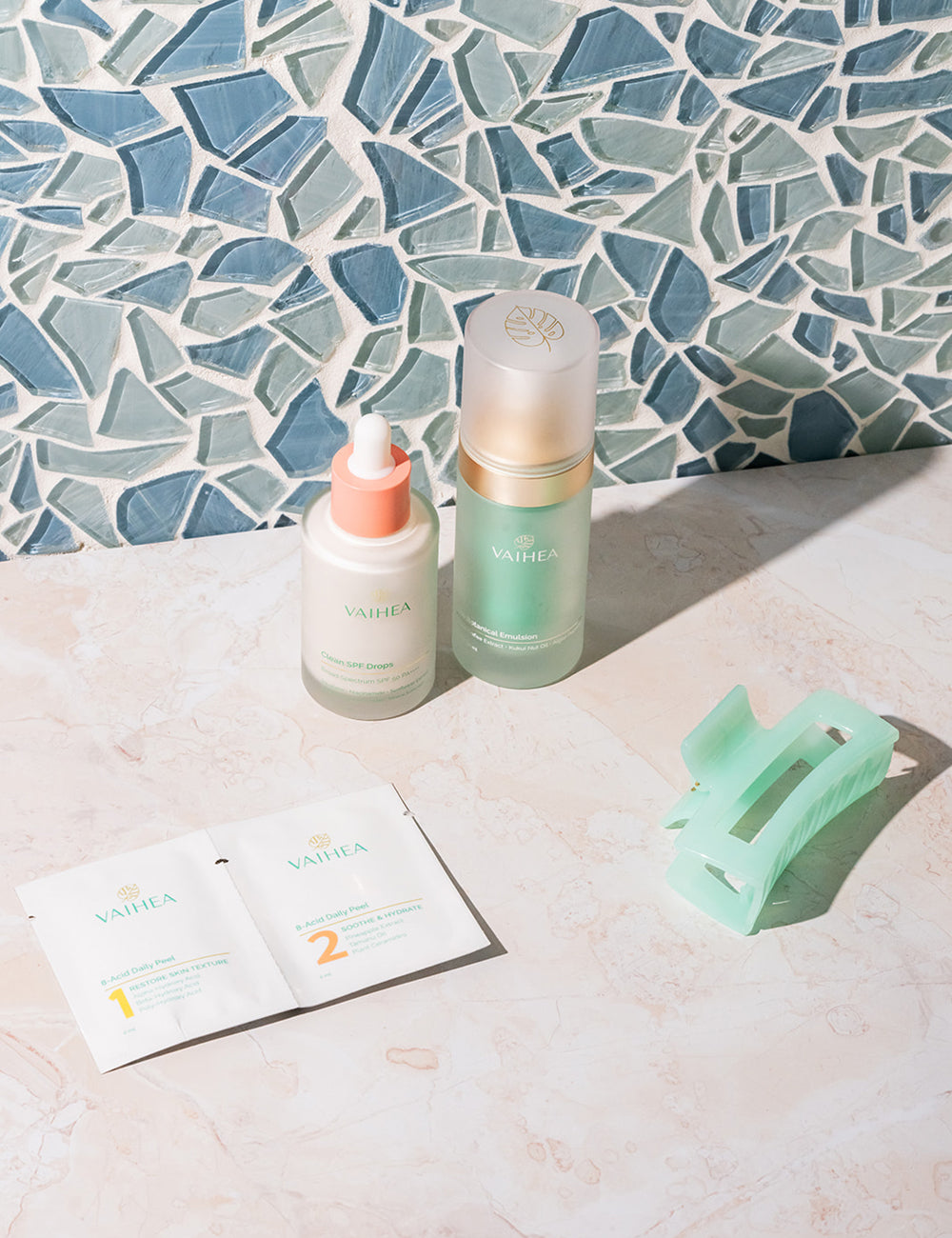 Two skincare products and a hair clip on a surface with a mosaic tile background