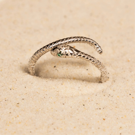 Silver snake-shaped ring with a green gemstone on a sandy background