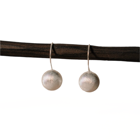 Pair of silver sphere earrings hanging on a dark brown rod against a white background