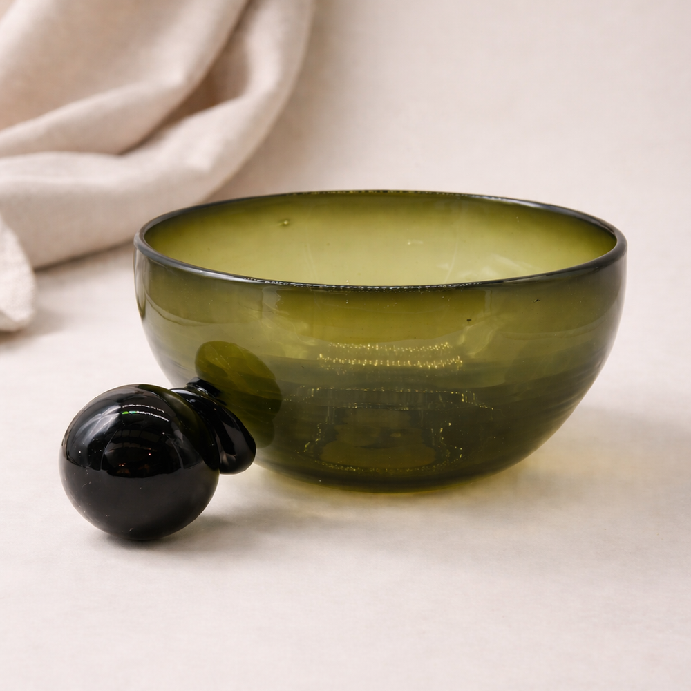 Green glass bowl with black handle on a light background
