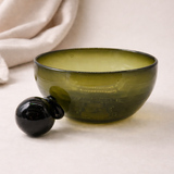 Green glass bowl with black handle on a light background