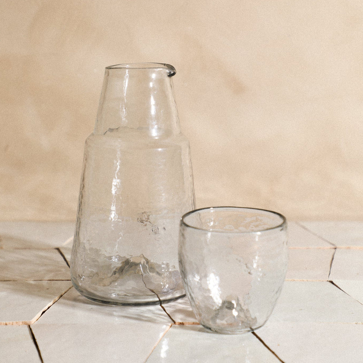 Two clear glass pieces on a tiled surface with a beige wall background