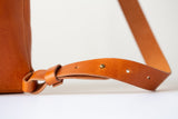 The Folded Backpack - Saddle. Close-up of a brown leather bag strap on a light background