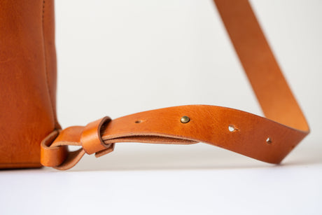 The Folded Backpack - Saddle. Close-up of a brown leather bag strap on a light background