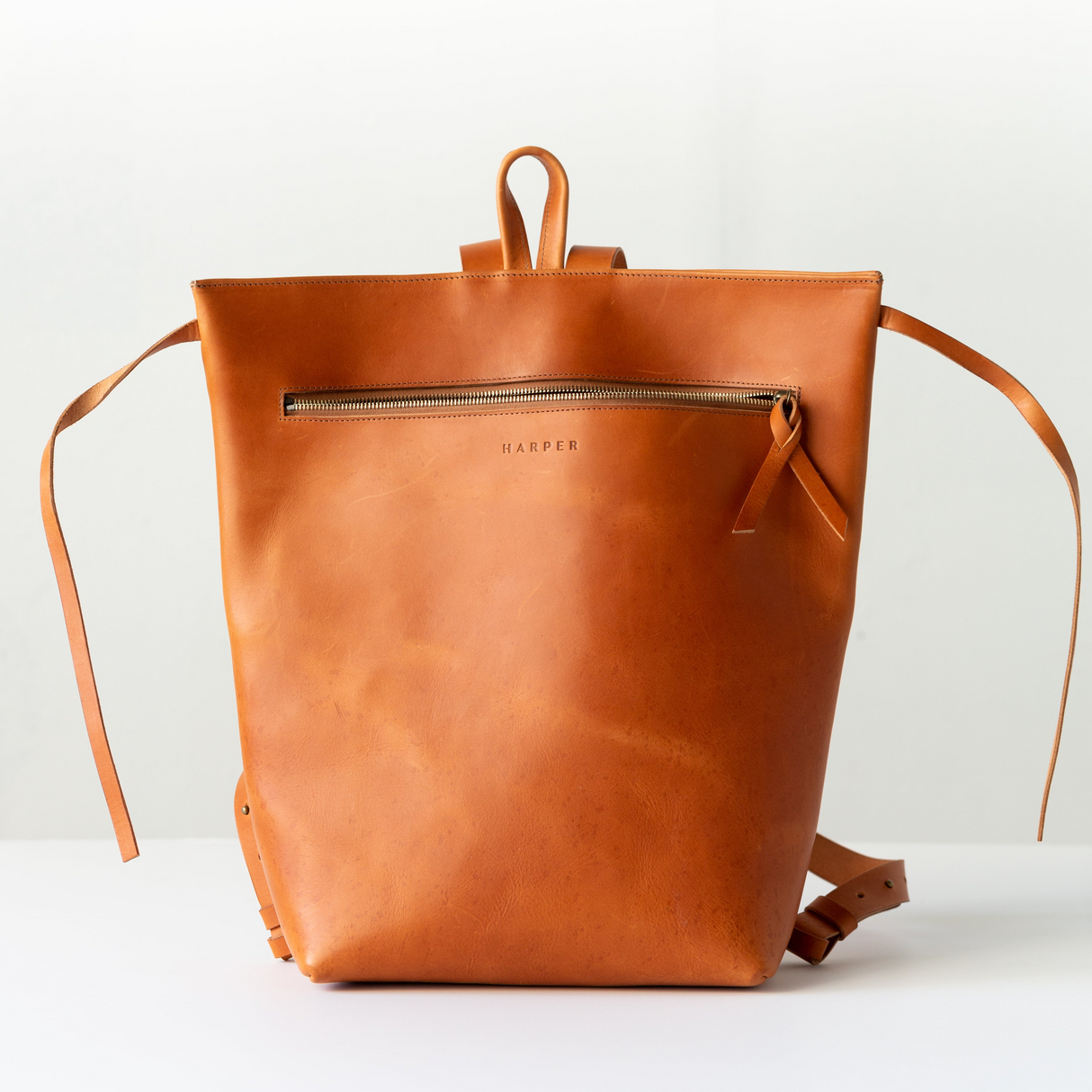 The Folded Backpack - Saddle. Brown leather backpack on a white background