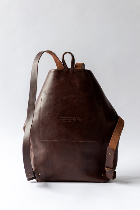 The Folded Backpack - Walnut. Brown leather backpack on a light gray background