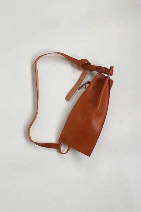The Offset Sling Bag - Saddle. Brown leather bag with a strap on a light gray background
