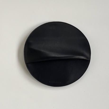 The Pleated Clutch - Black. Black circular product with 'Harper' branding on a light gray background