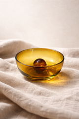 Amber glass bowl with a sphere on a beige fabric background